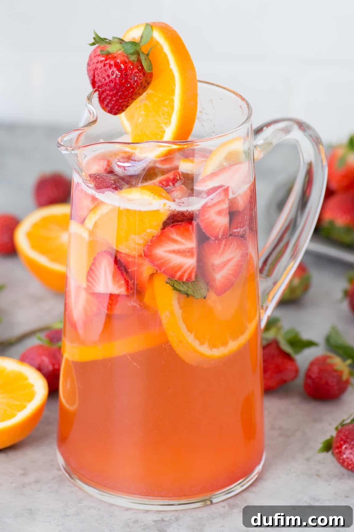 A glass pitcher filled with homemade strawberry sangria, brimming with sliced strawberries, oranges, and fresh mint, ready to be served.