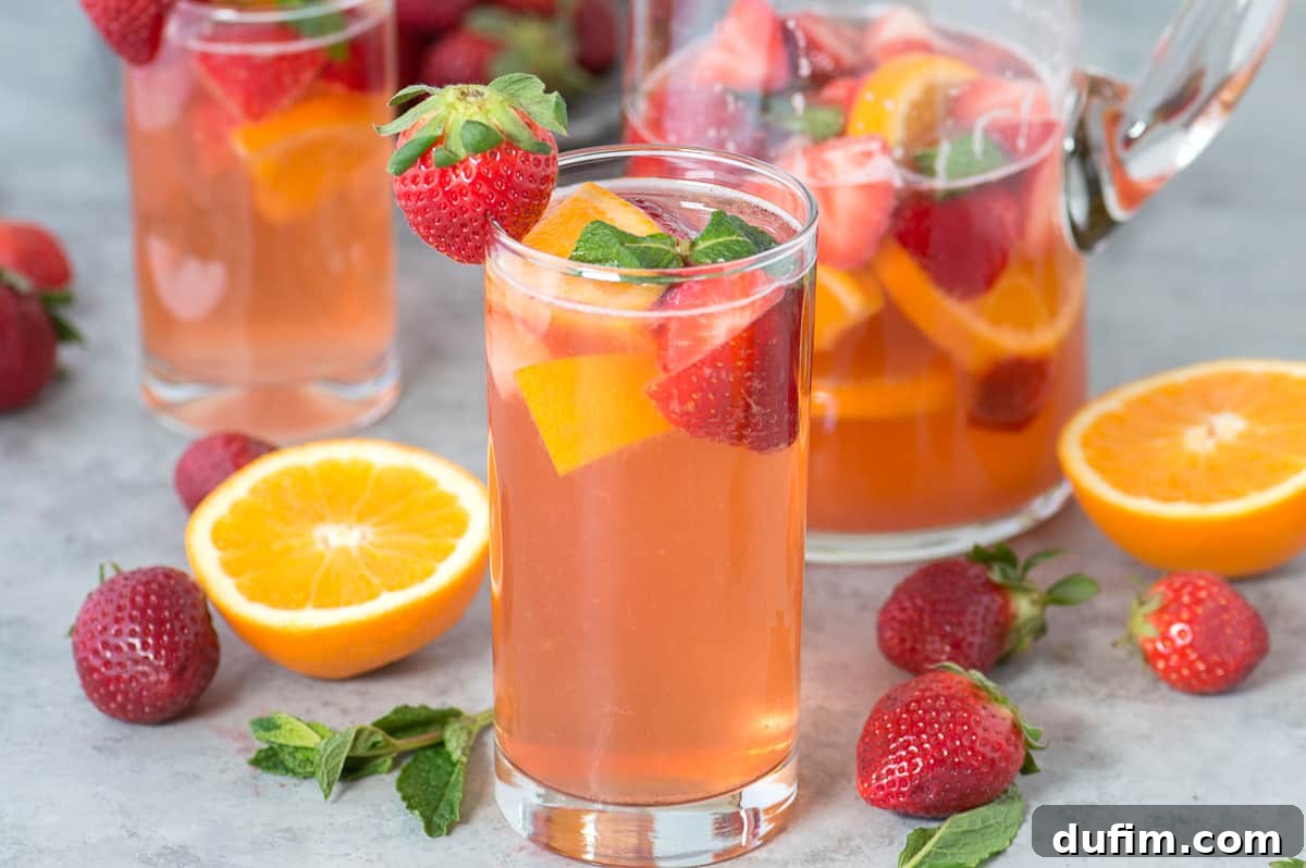 A close-up of strawberry sangria in a clear glass, showing the rich red color and fresh fruit garnishes.