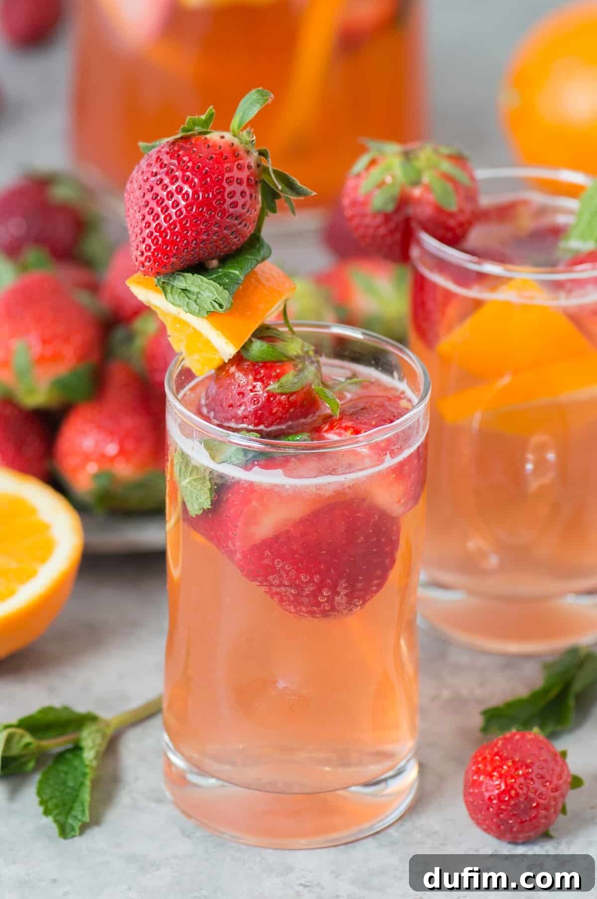 A glass of strawberry sangria with a fruit skewer, showcasing fresh strawberries, orange, and mint for garnish.