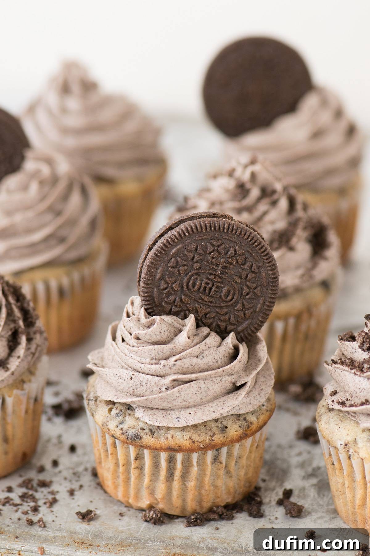 A perfectly frosted cookies and cream cupcake adorned with a whole Oreo cookie on top, presented on a rustic metal plate.