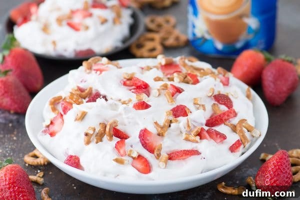 Overhead view of Strawberry Pretzel Fluff Salad in a white serving bowl, garnished with whole strawberries and more pretzel pieces, emphasizing its delightful presentation.