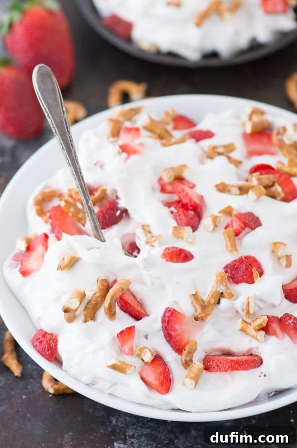 A top-down shot of a large glass bowl filled with Strawberry Pretzel Fluff Salad, highlighting its creamy texture and the abundance of fresh strawberries.