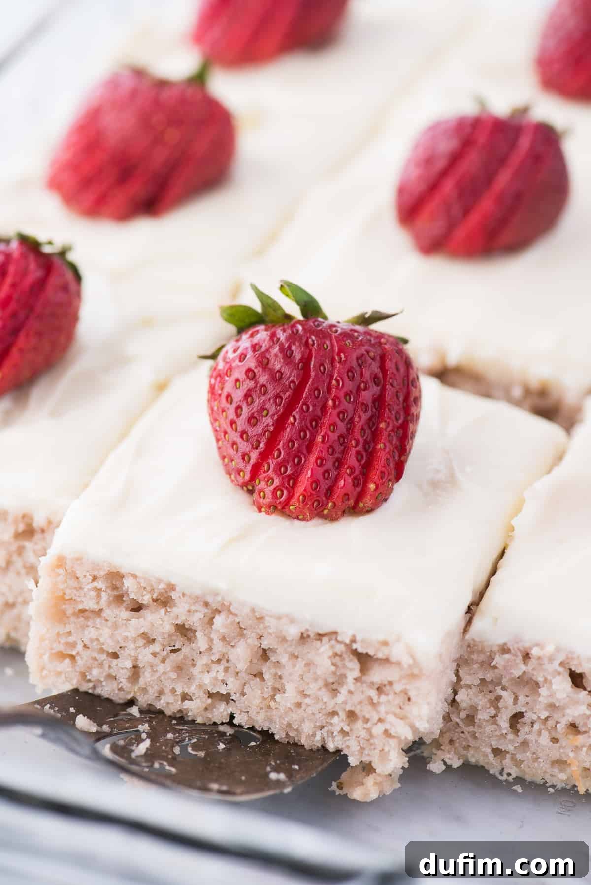 A perfectly portioned slice of strawberry cake with thick cream cheese frosting and a fresh strawberry wedge, served on a metal spatula, ready to be plated.