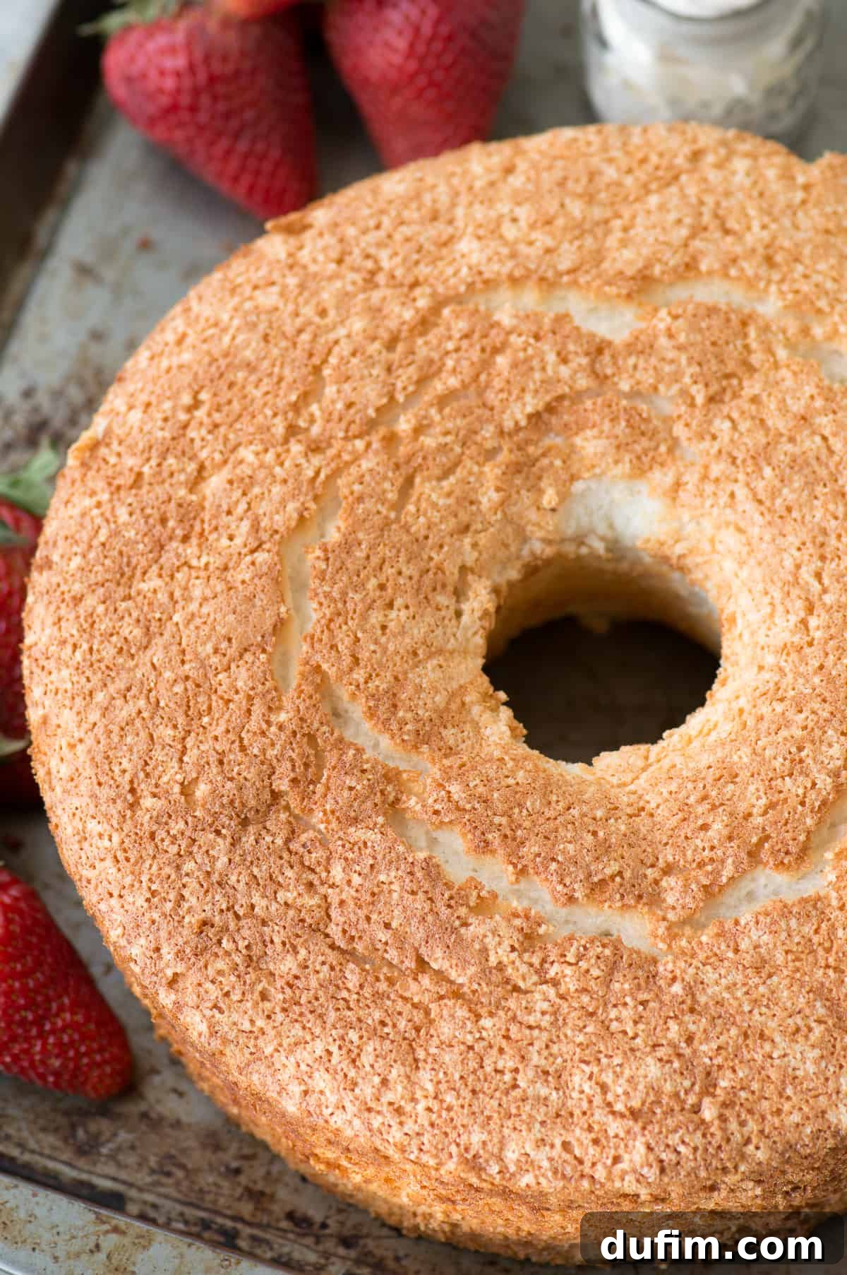 Heavenly Homemade Angel Food Cake 4 A close-up of the delicate, porous texture of a slice of homemade angel food cake, glistening with a light sugar dusting, showcasing its perfect rise and airy structure. This recipe makes it simple to bake with regular all-purpose flour.