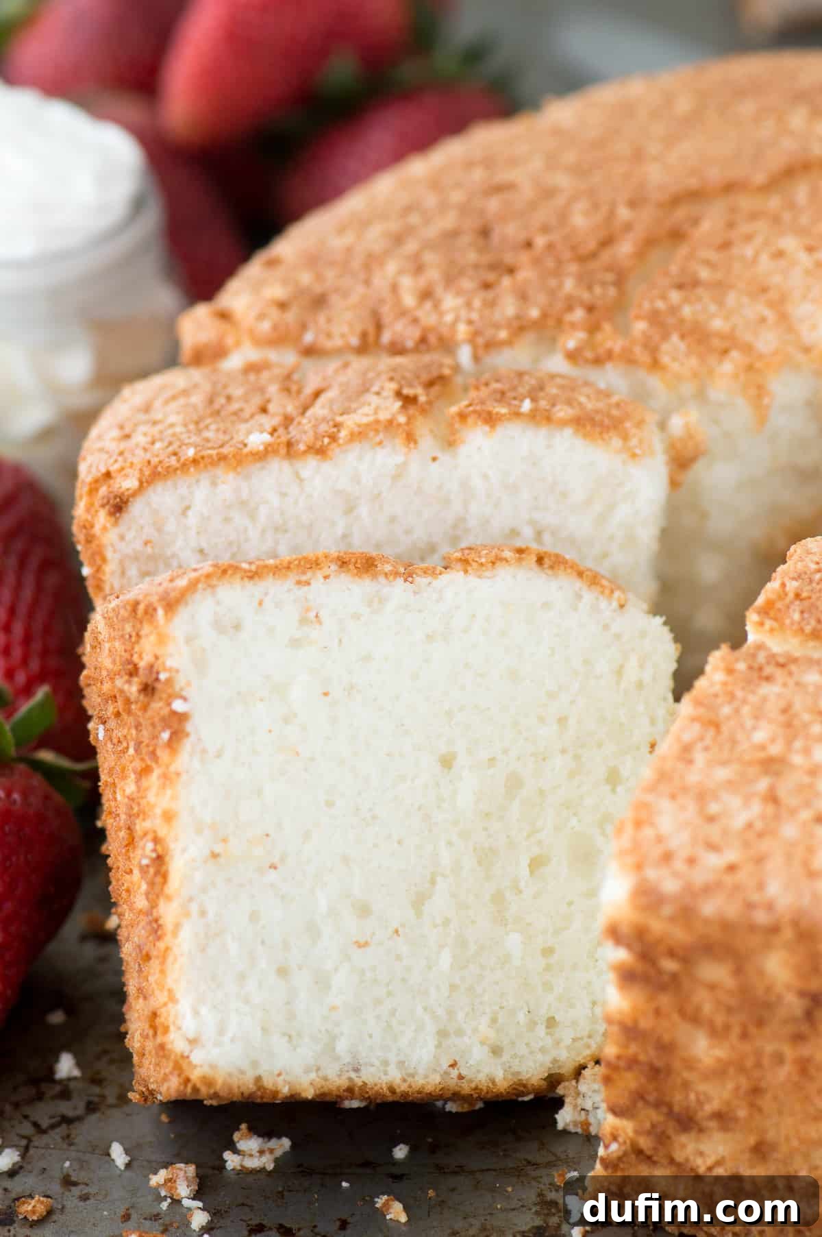 Heavenly Homemade Angel Food Cake 5 Several slices of homemade angel food cake are arranged on a rustic wooden board, some topped with whipped cream and fresh strawberries, highlighting the versatility and deliciousness of this easy, no-cake-flour recipe.