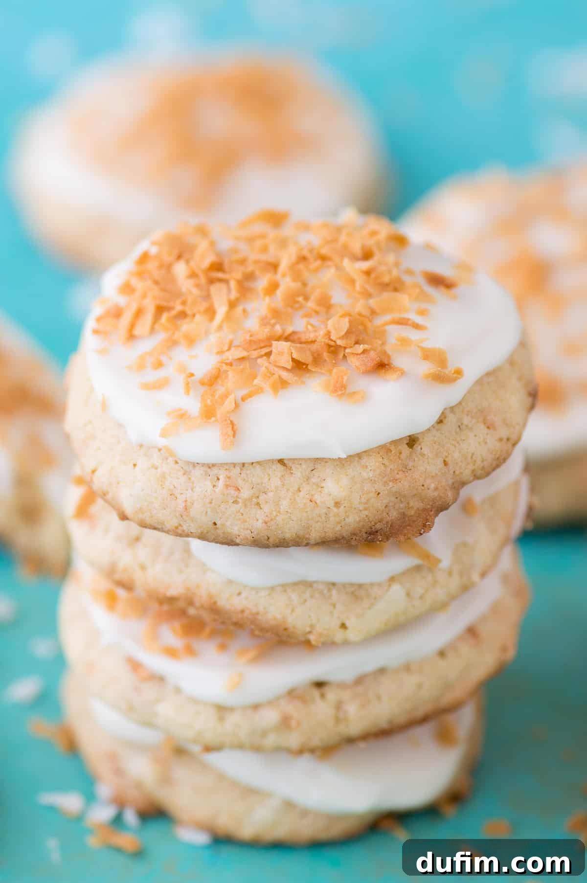 Stack of coconut cookies with white frosting on a teal background