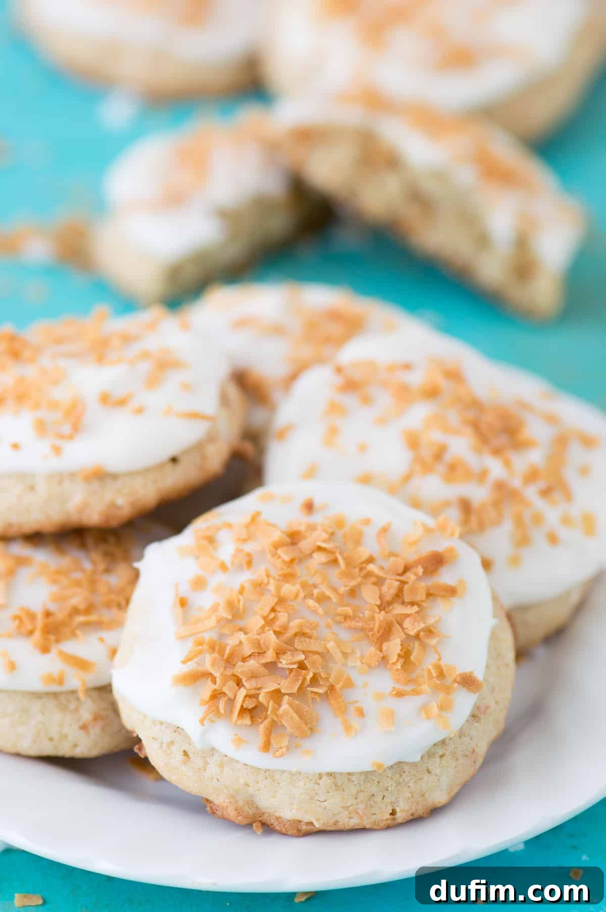 Coconut cookies with white frosting on a white plate on teal background