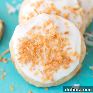 A round coconut cookie topped with white icing and sprinkled with toasted coconut flakes, set on a bright turquoise background.