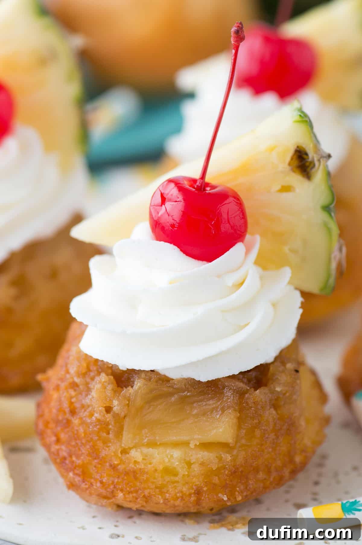 Mini pineapple upside down cakes with whipped cream, a cherry and pineapple slice on white plate, ready to be served.