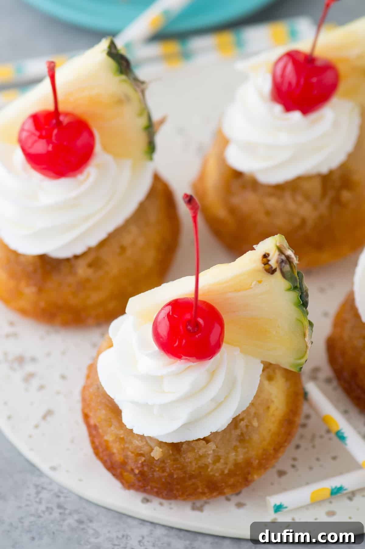 Mini pineapple upside down cakes with whipped cream, a cherry and pineapple slice on white plate, ready for a tropical treat.