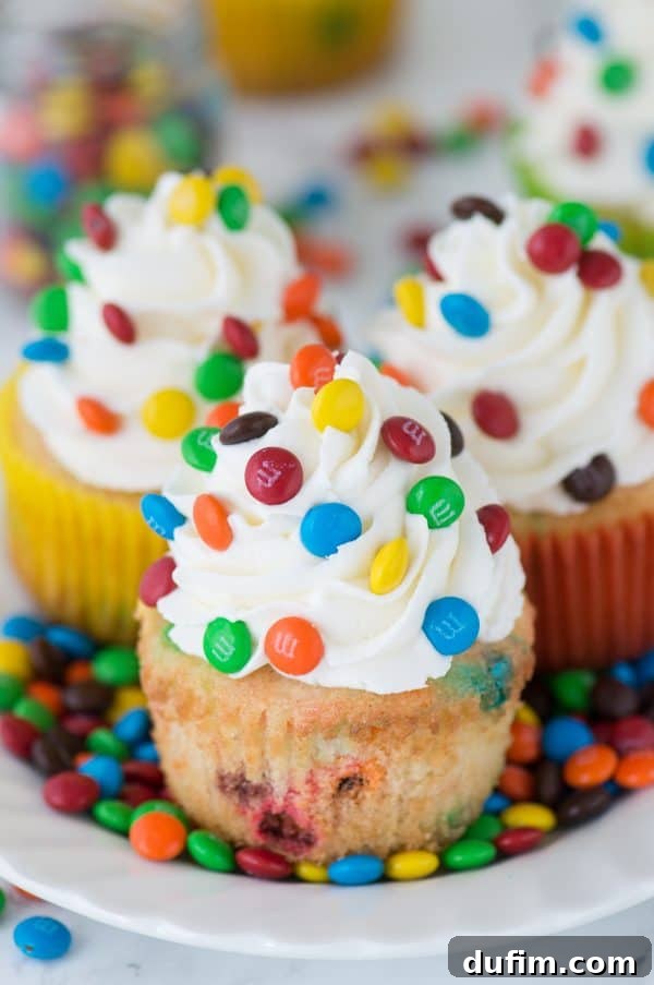 Delicious M&M cupcakes, featuring a moist vanilla cake base with mini M&Ms baked into the batter, topped with a smooth vanilla buttercream and additional candies.