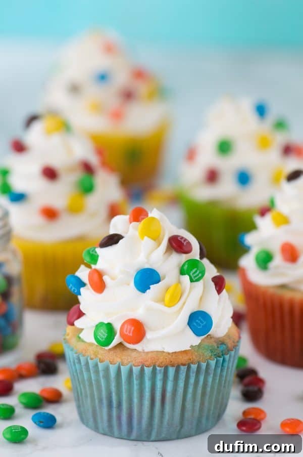 M&M vanilla cupcakes, showcasing a close-up of the vibrant candy-coated chocolates on top of creamy white frosting.