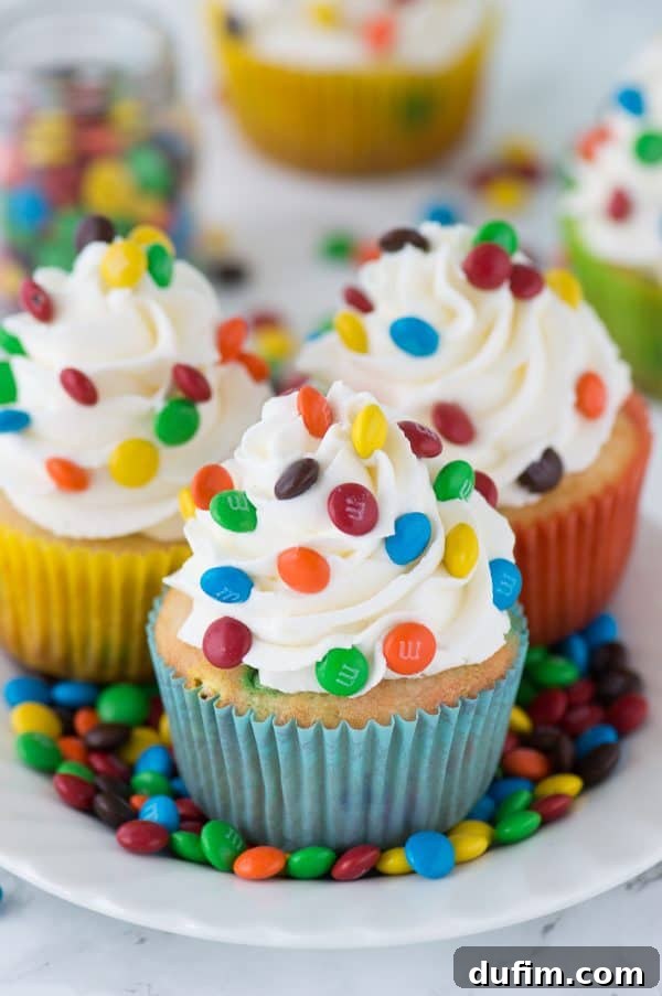 M and M Cupcakes 6 A stunning close-up of a loaded M&M cupcake, showcasing its moist vanilla cake and generous vanilla buttercream frosting topped with an abundance of colorful mini M&Ms.