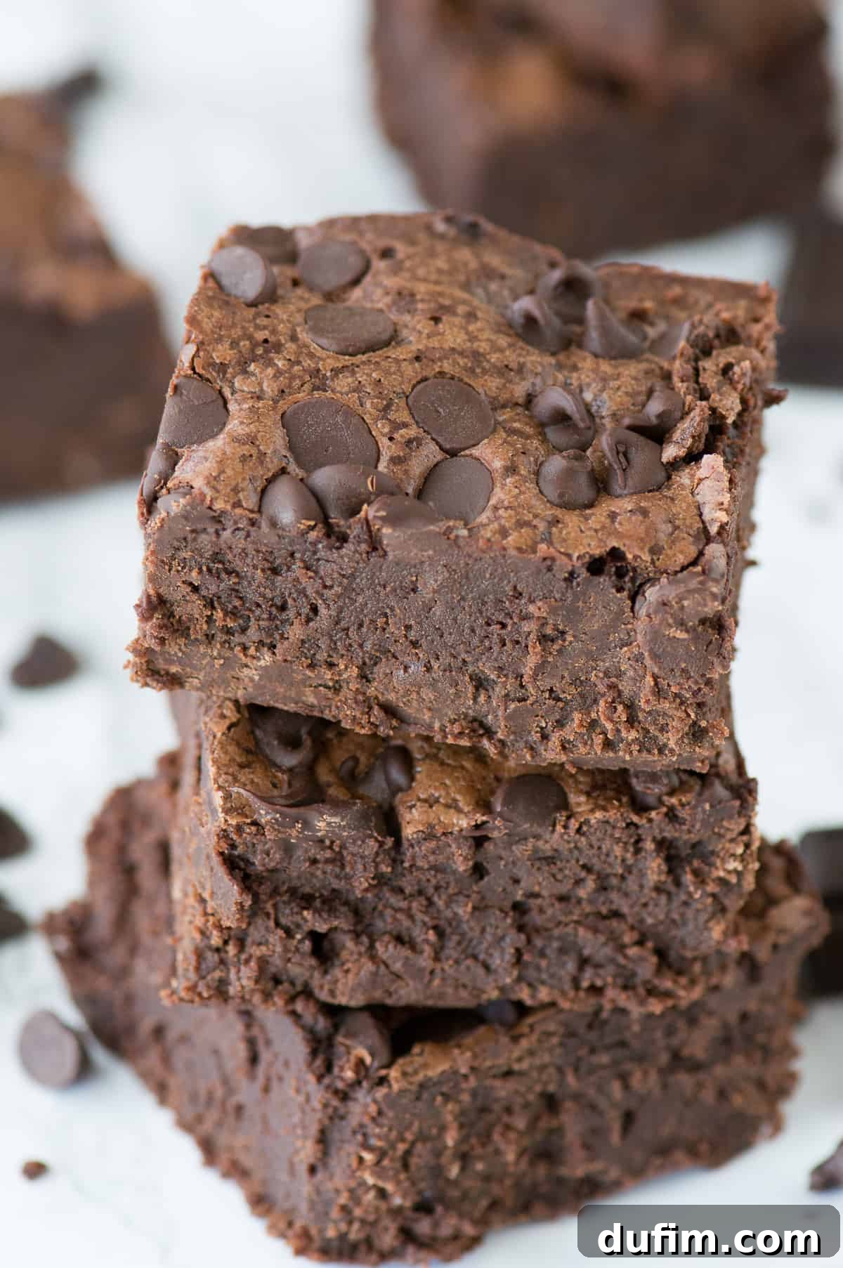 Decadent Fudge Brownies 3 three super fudgy brownies stacked on top of each other on a white background, highlighting their rich color and texture