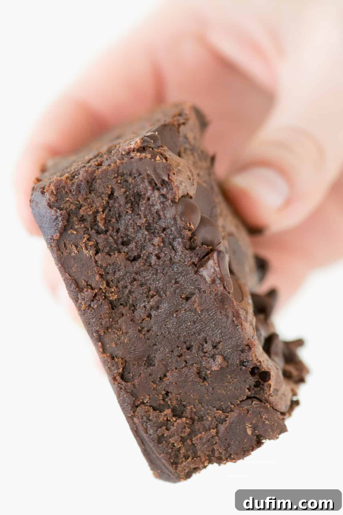 Decadent Fudge Brownies 4 hand holding one super fudgy brownie on a white background, demonstrating its delightful texture