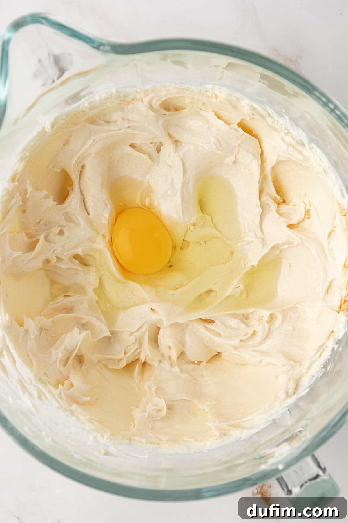 An egg being gently mixed into the cheesecake batter, ensuring minimal air incorporation.