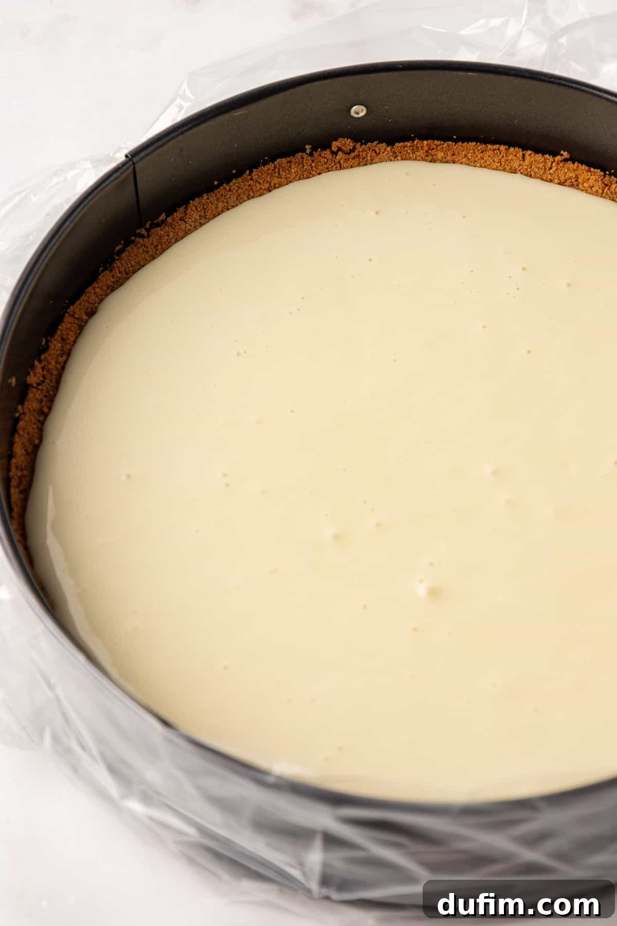The smooth cheesecake batter being carefully poured over the cooled graham cracker crust in the springform pan.