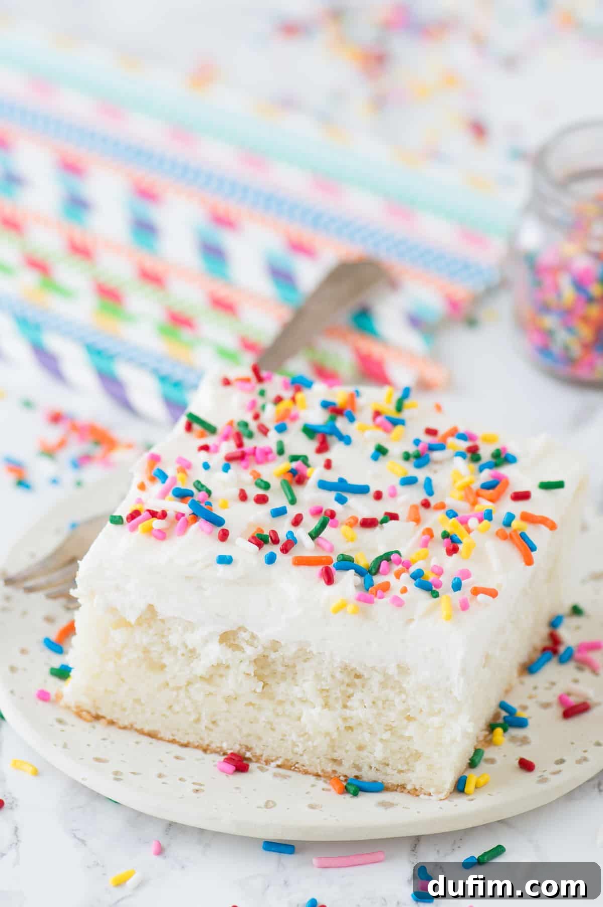 Delicious white cake adorned with vibrant funfetti sprinkles, served on a crisp white plate, showcasing its moist texture and inviting appearance.