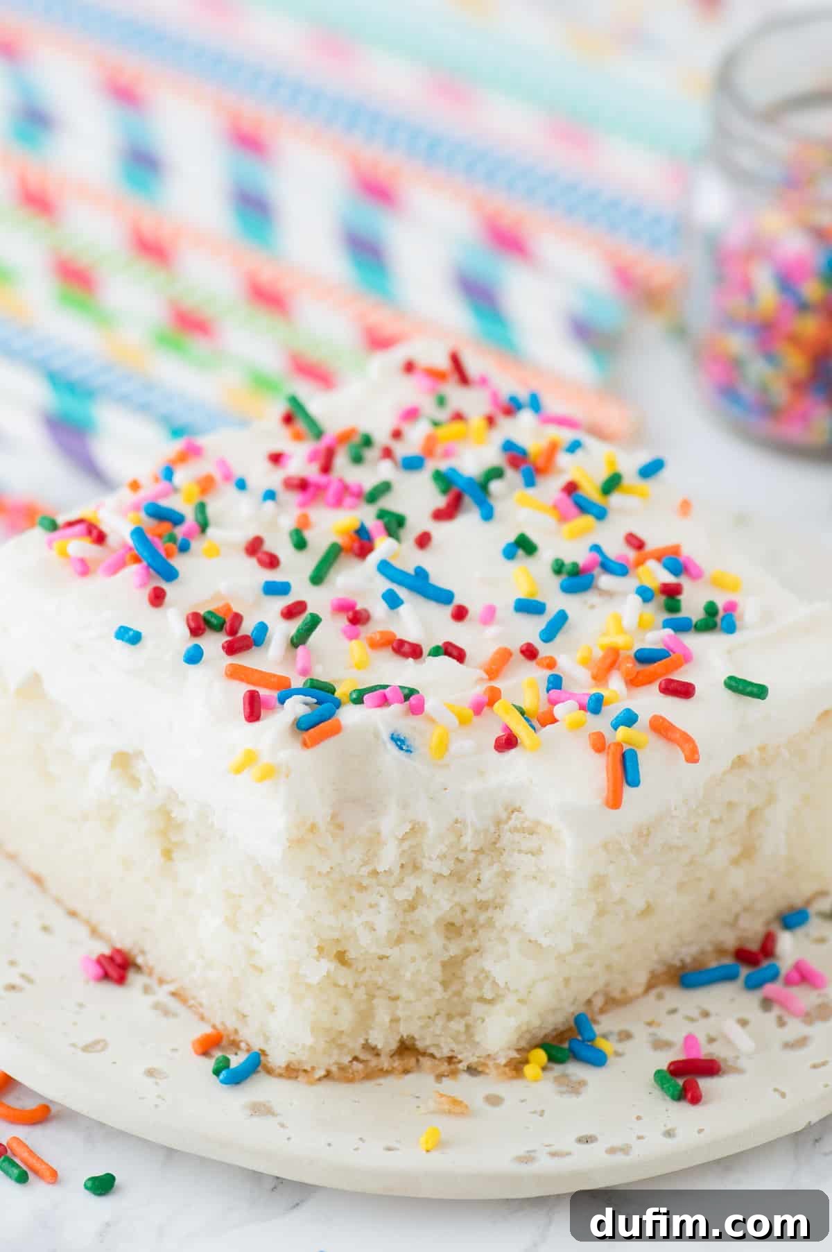 Close-up of a delectable slice of white cake with colorful funfetti sprinkles, a bite removed to reveal its incredibly moist and tender crumb texture.