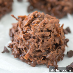 Close-up of an espresso coconut macaroon cookie with a rough, textured surface, sitting on white parchment paper with a few scattered chocolate chips nearby.