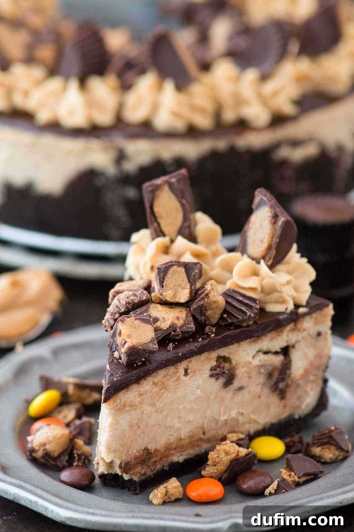 A glorious slice of Reese's cheesecake, adorned with chocolate ganache and extra Reese's cups, presented on an elegant metal plate.