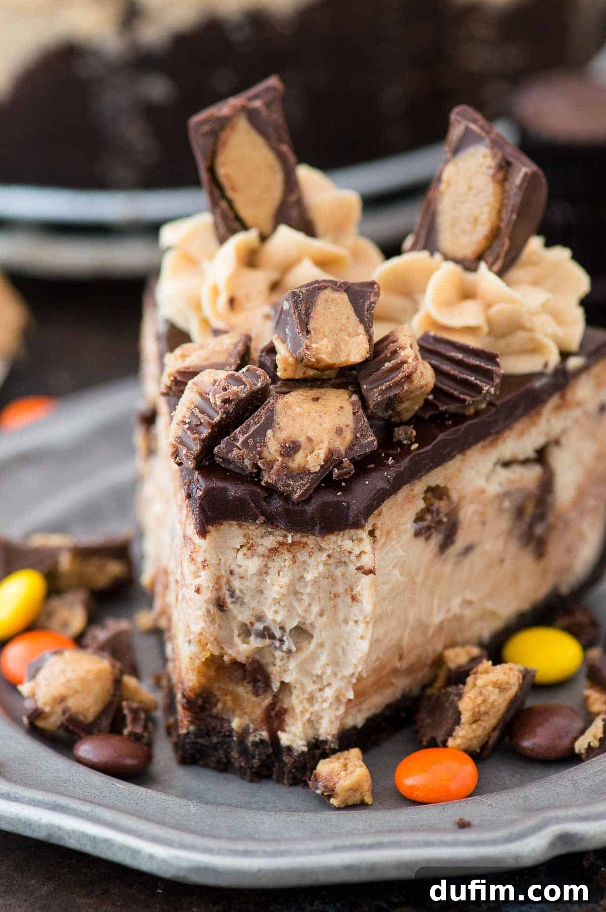 Another beautiful slice of Reese's cheesecake, richly topped with chocolate ganache and mini Reese's cups, served on a metal plate.