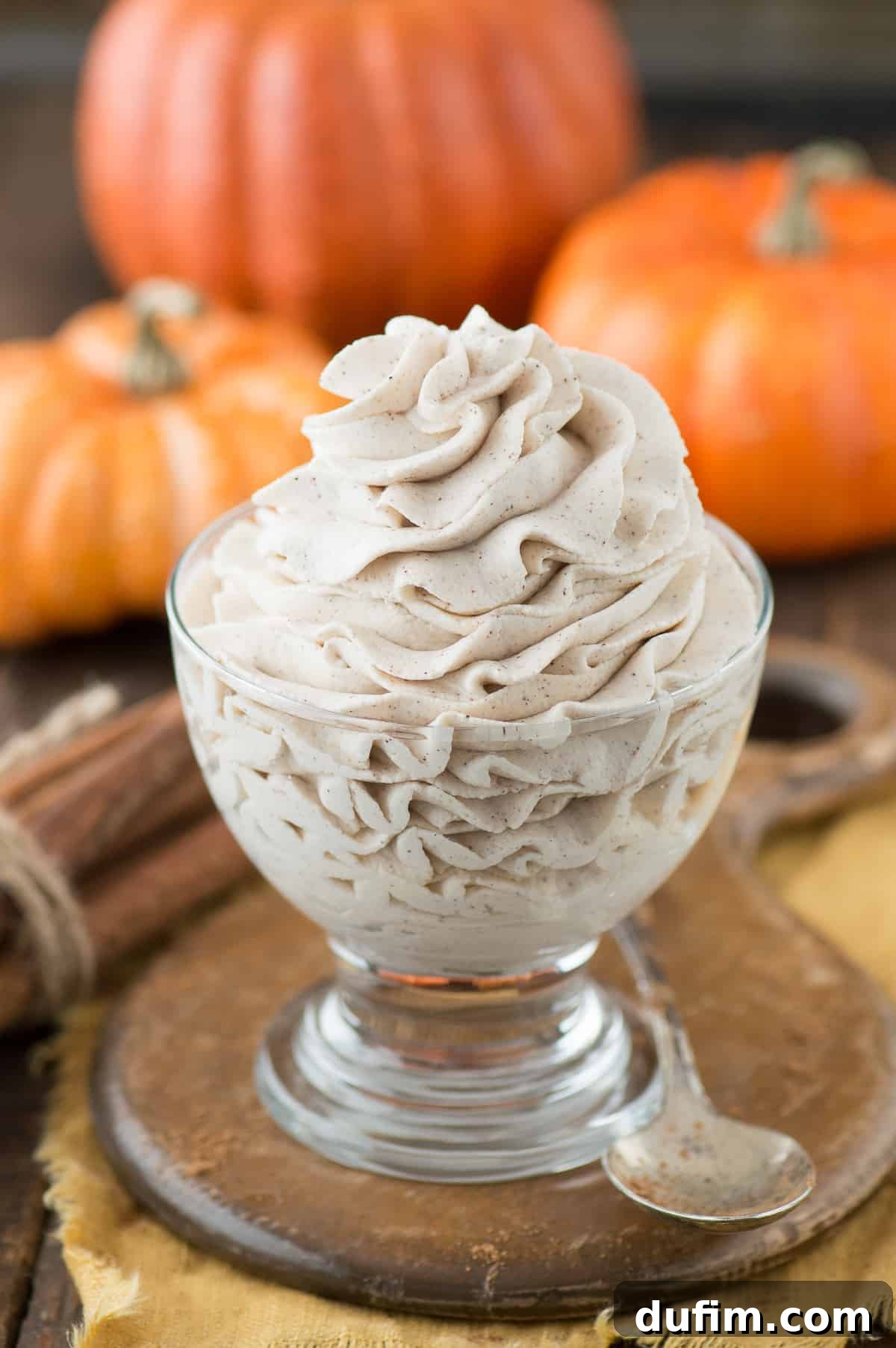 A generous swirl of homemade pumpkin whipped cream piped into a clear glass bowl, set against a rustic wooden background, inviting a taste of fall.