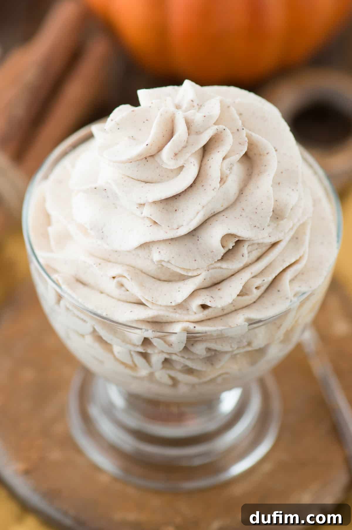 A close-up view of freshly made pumpkin whipped cream, generously piped into a clear bowl on a wooden surface, showcasing its delightful texture.