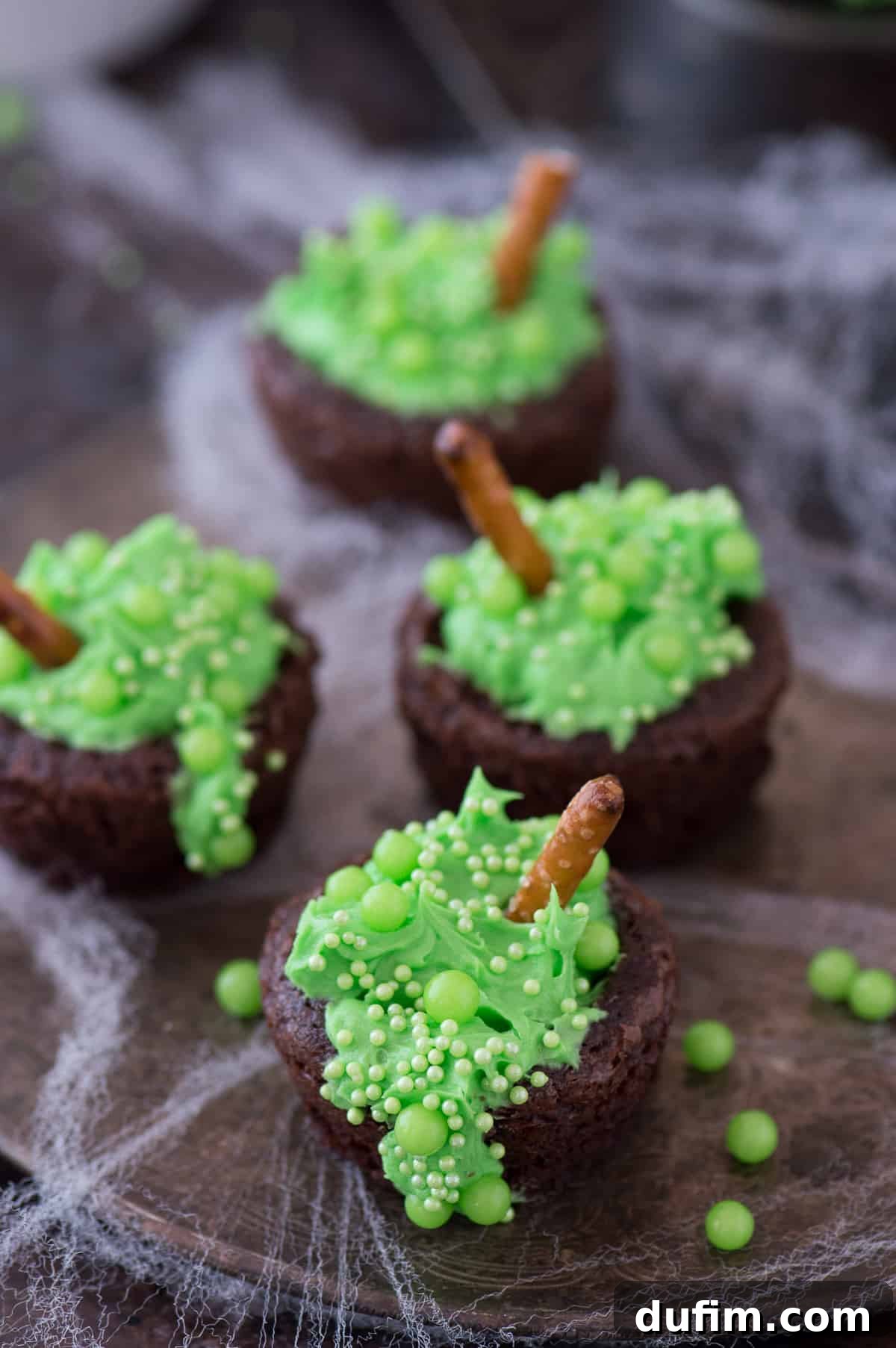 A vibrant display of Bubbling Witch's Cauldron Brownies, showcasing their bright green frosting, various green sprinkles, and pretzel stick stirrers, ready for a Halloween gathering.