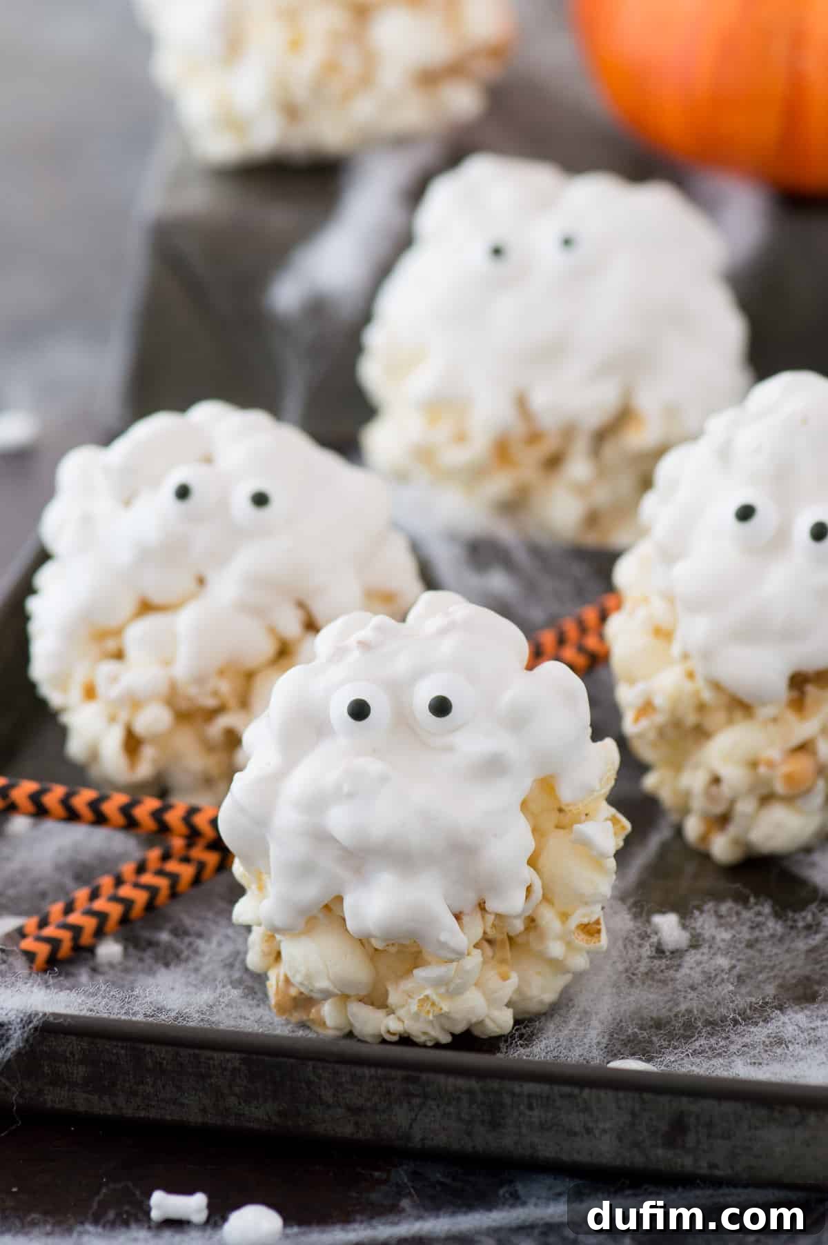 White chocolate-covered popcorn balls with candy eyeballs arranged to resemble friendly ghosts, presented on a dark background with subtle Halloween decorations.