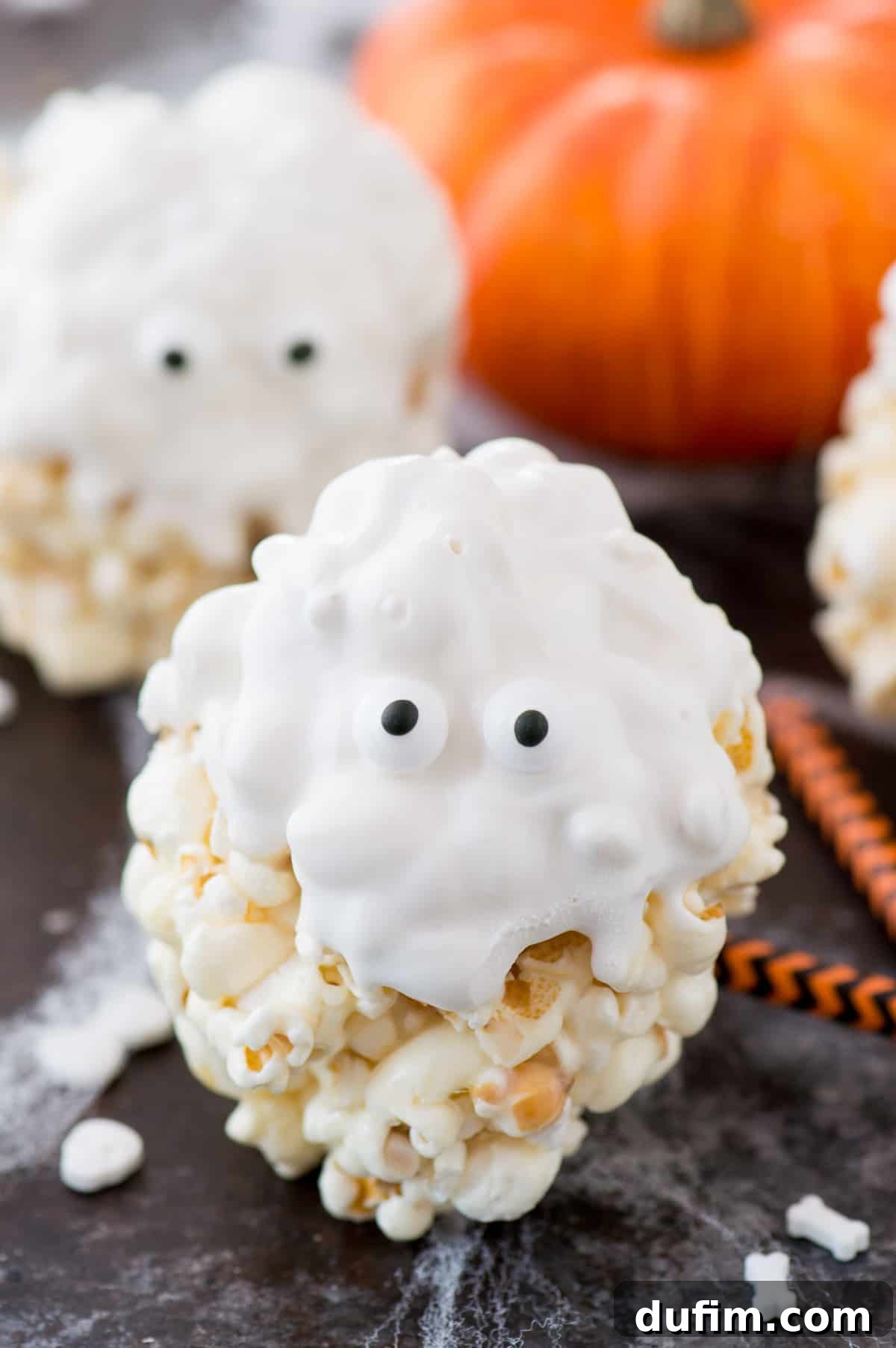 Close-up of a ghost popcorn ball, showcasing its smooth white chocolate coating and two perfectly placed candy eyeballs, emphasizing its fun and simple design.