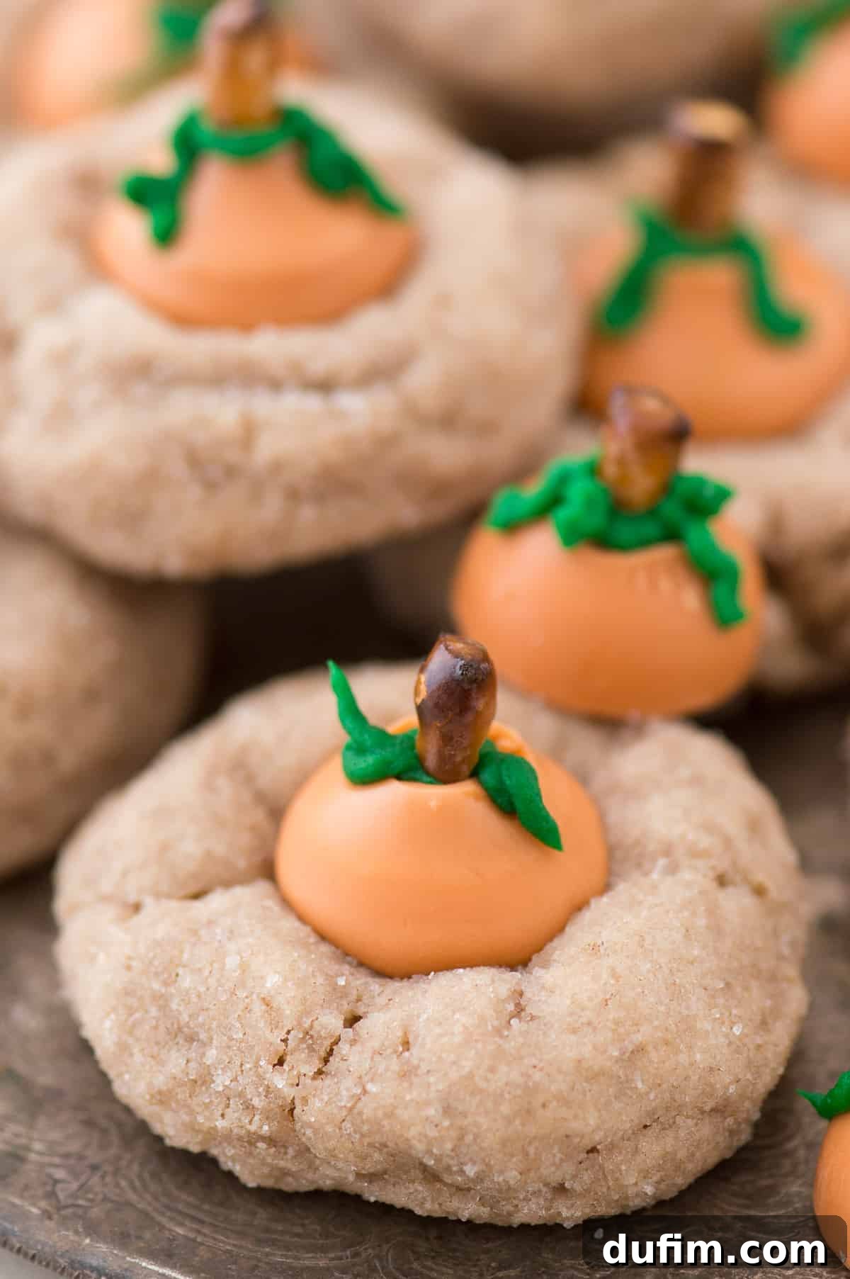 Pumpkin Blossom Delights 2 A close-up shot of several pumpkin blossom cookies on a white plate, showcasing their cute pumpkin design with green frosting leaves and pretzel stems, ready for fall enjoyment.