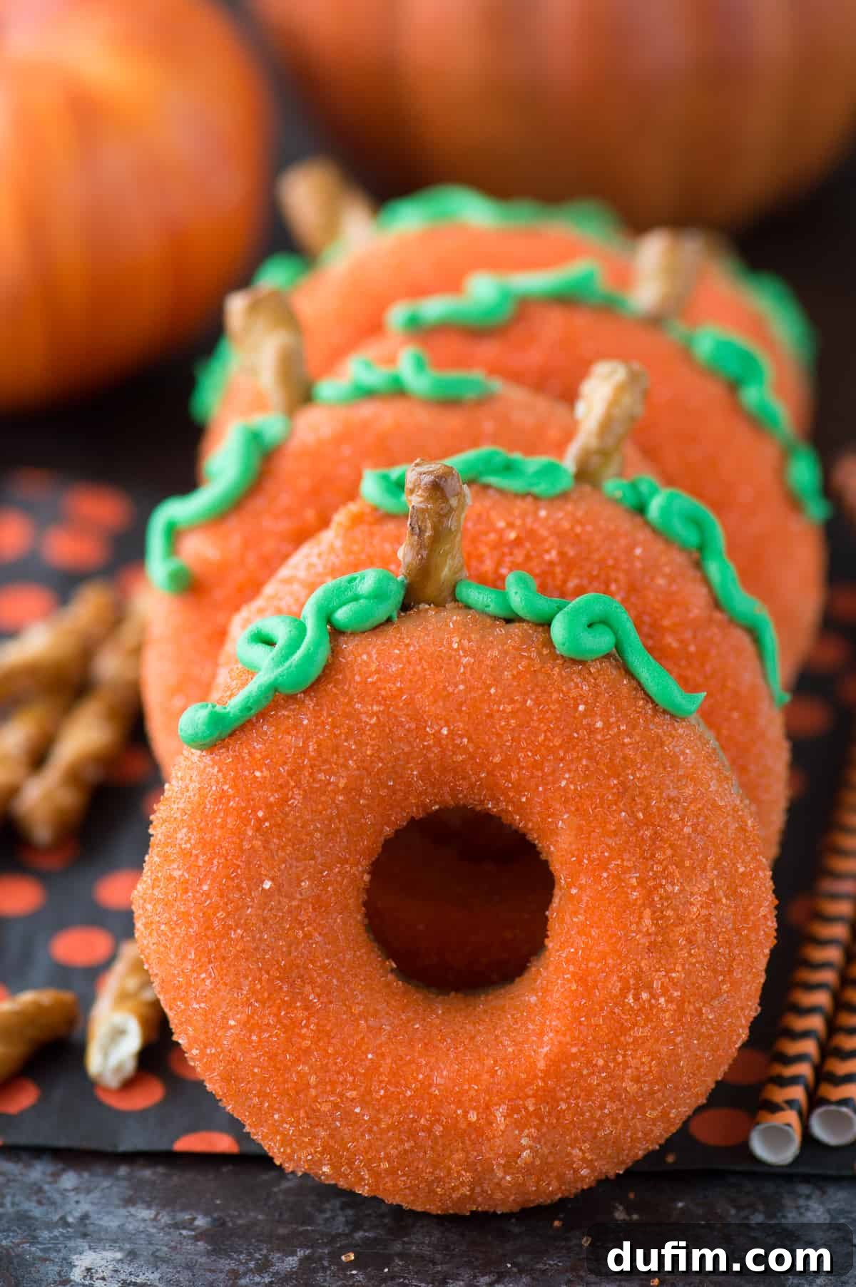 Golden Pumpkin Puffs 3 Close-up of a pumpkin donut showing its detailed orange candy melt glaze, green frosting, and pretzel stem, highlighting the autumnal theme.