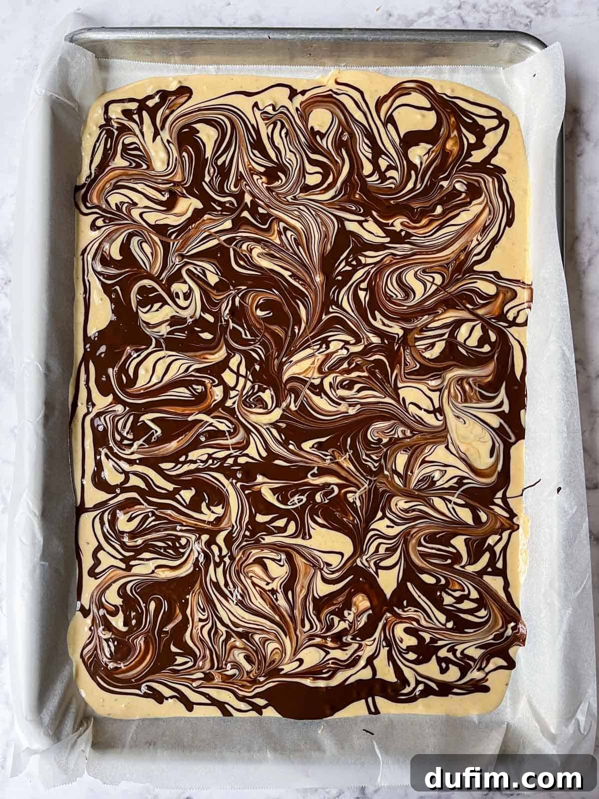 A large slab of tiger butter bark set on a baking sheet, ready to be broken into pieces, displaying vibrant swirls.