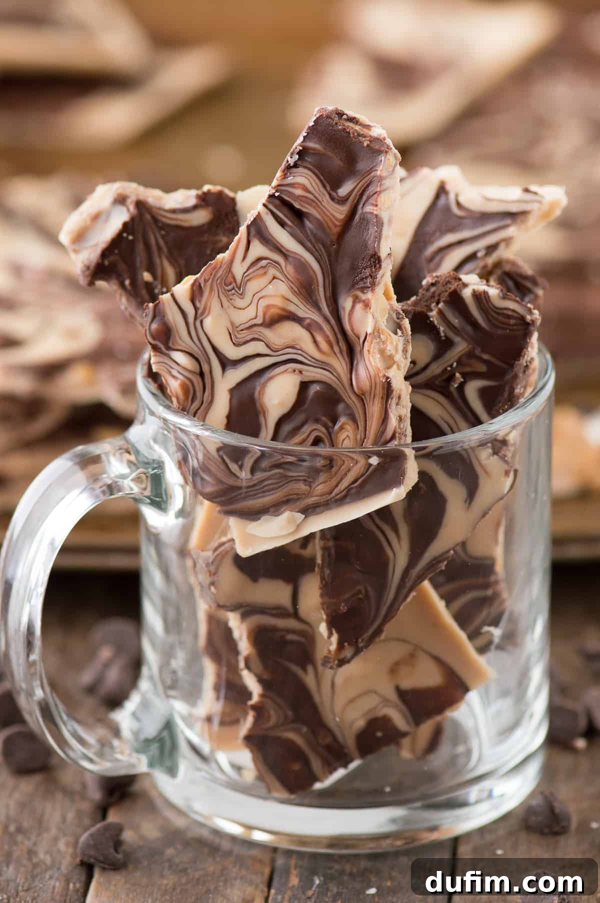 Pieces of tiger butter bark displayed artfully in a clear mug against a warm wood background, highlighting its marbled beauty.