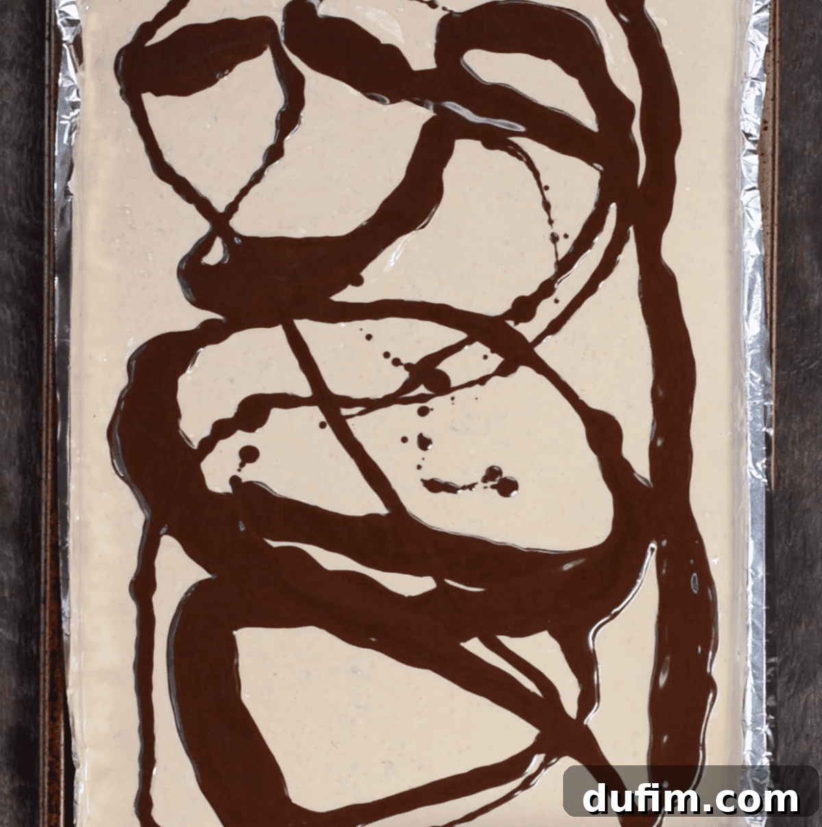 Beginning to swirl the melted chocolate into the peanut butter almond bark mixture on a baking sheet to create tiger stripes.
