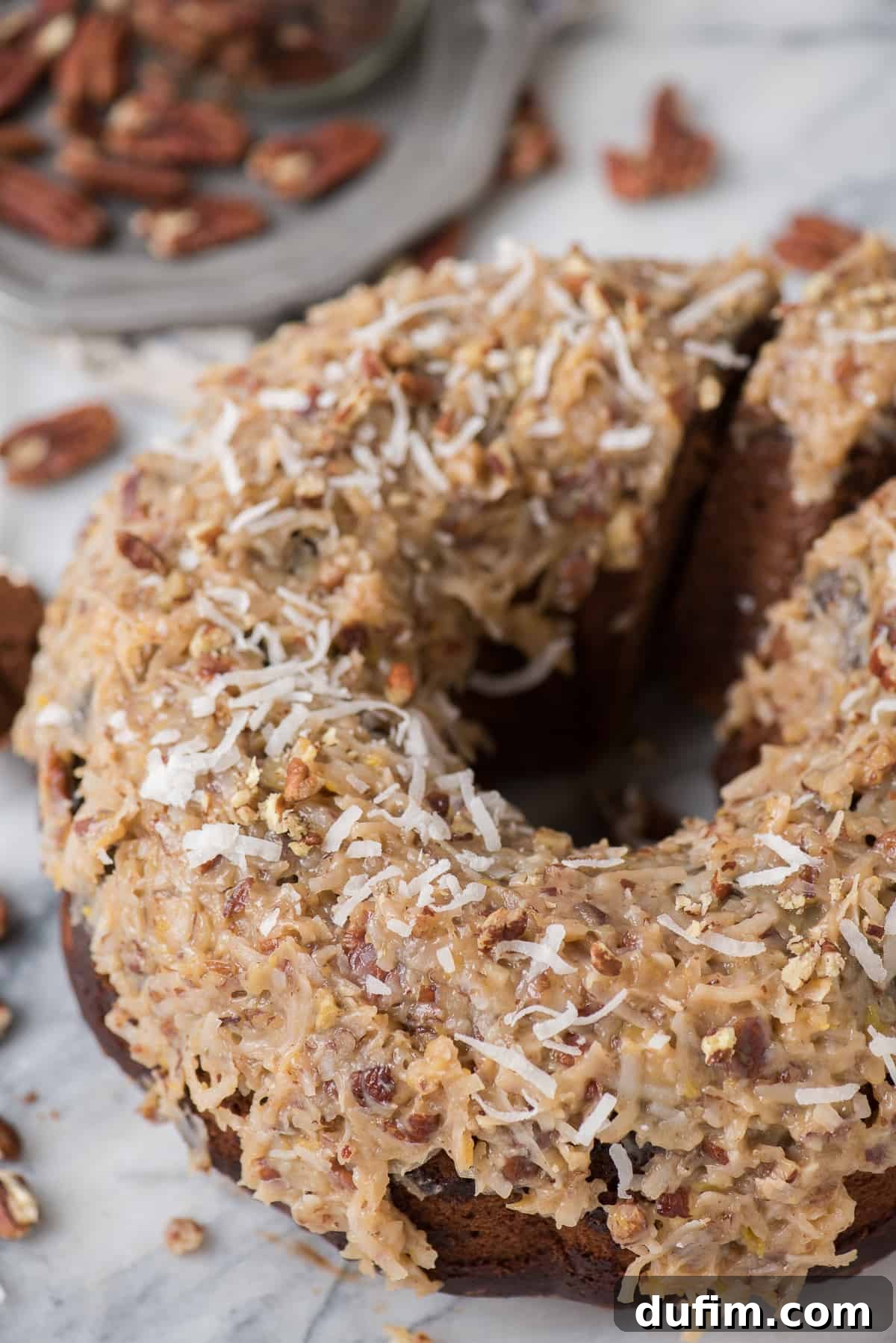 A close-up of a slice of German Chocolate Bundt Cake showcasing its moist interior and generous, golden-brown coconut pecan frosting. The texture and richness are clearly visible, promising a delightful experience.