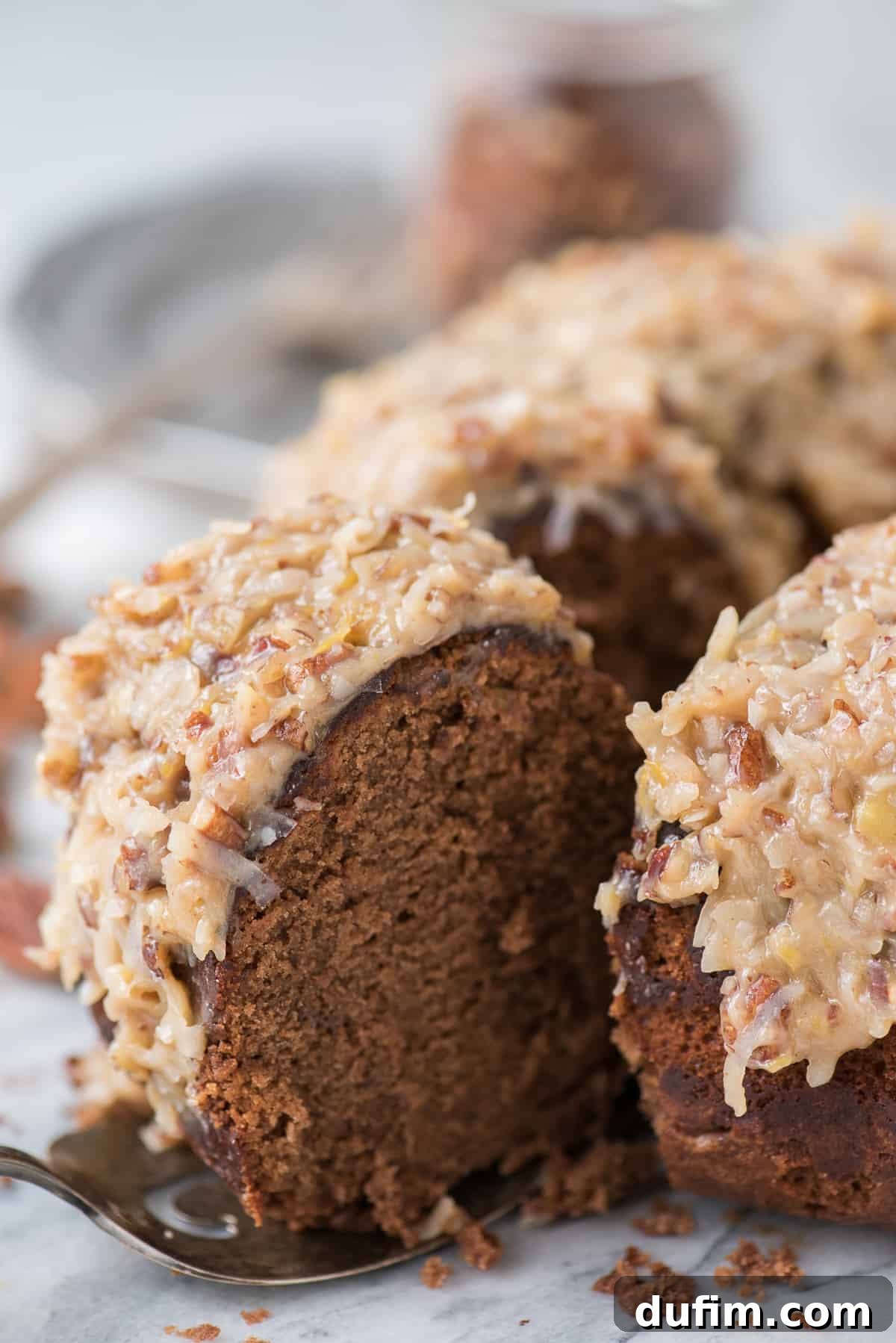An overhead shot of the full German Chocolate Bundt Cake, showcasing its intricate bundt shape, perfectly golden frosting, and scattered pecan pieces. The presentation is elegant and inviting, highlighting the cake's homemade appeal.