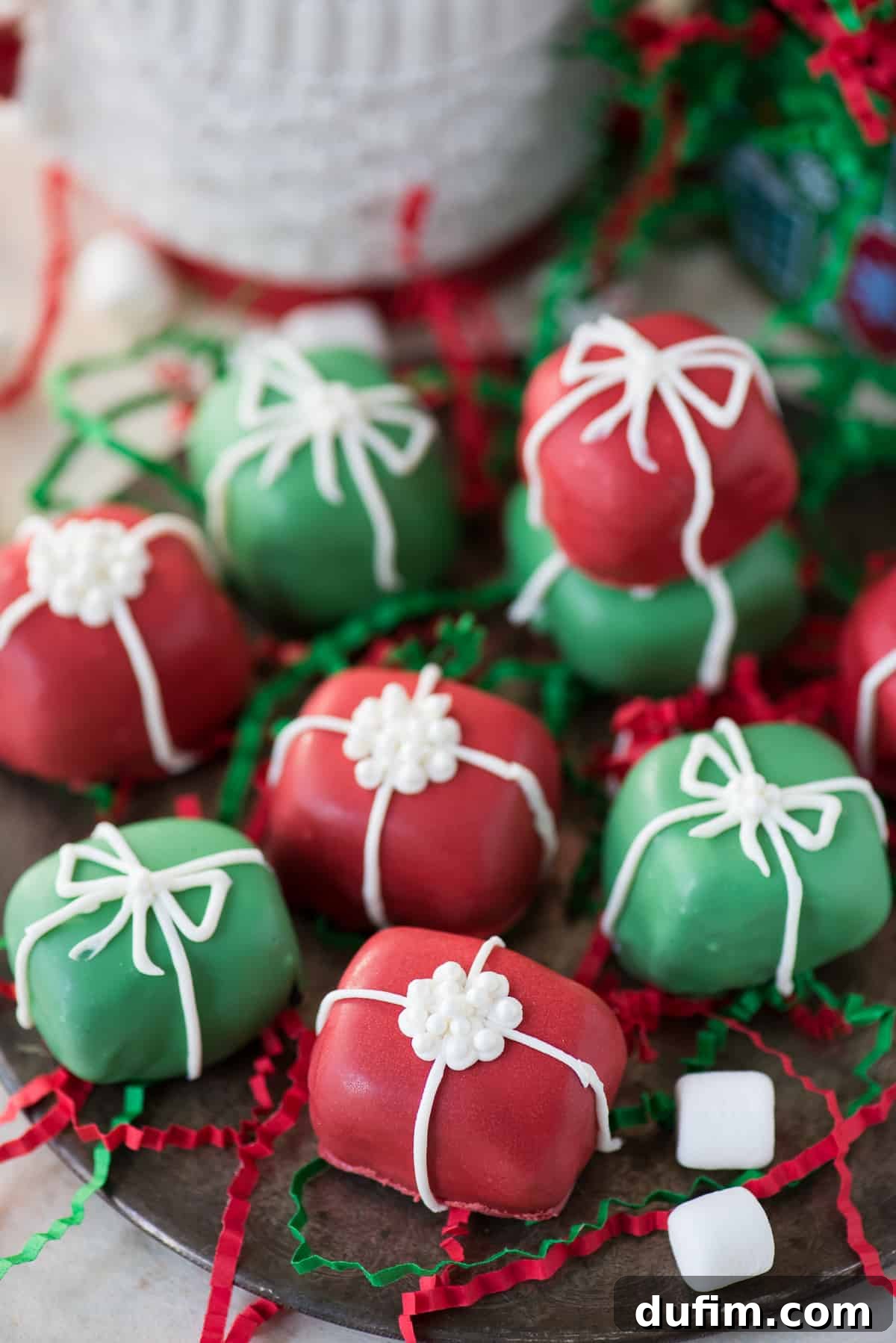Red and green Oreo balls shaped as Christmas presents with white bows on a metal plate, ready for holiday gifting.