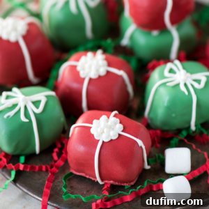 Colorful Christmas Oreo balls decorated like presents, with red and green icing, white icing bows, and flower-shaped accents. Some mini marshmallows and festive shredded paper surround these cheerful treats.