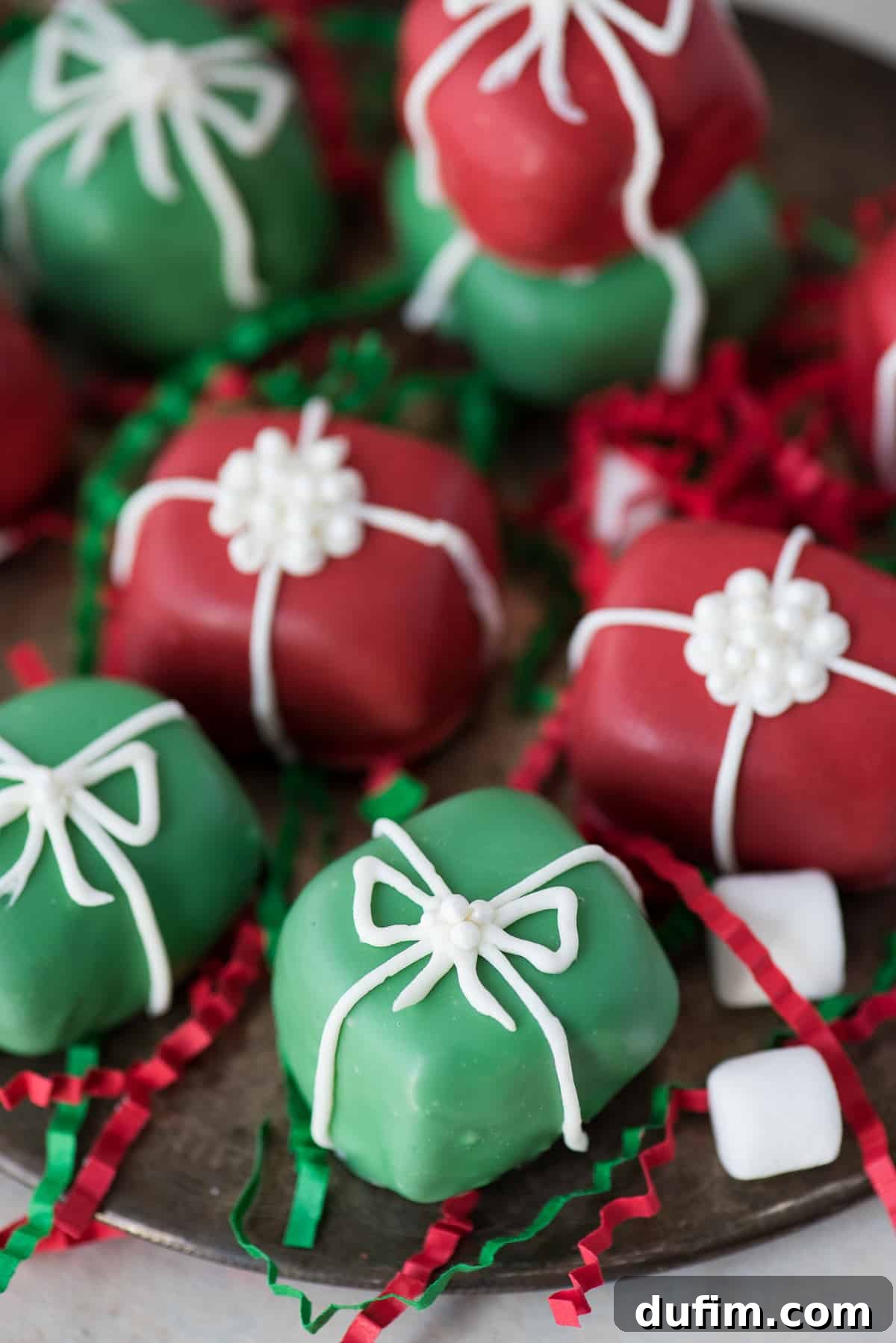 A close-up of red and green Christmas present Oreo balls adorned with elegant white bows, arranged beautifully on a metal serving plate.