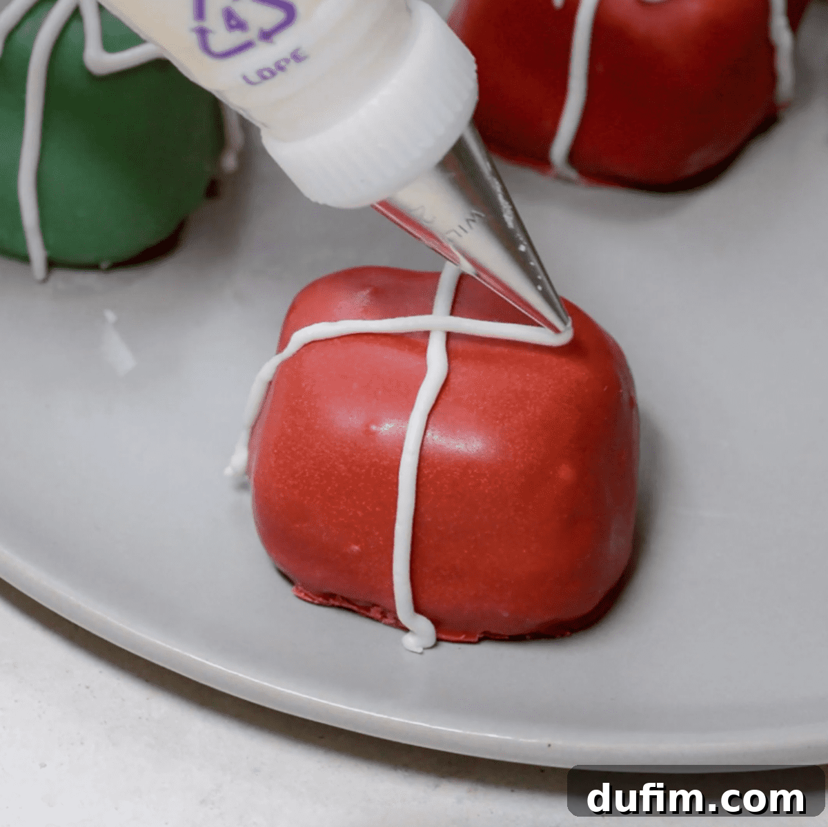 A steady hand piping a delicate white bow onto a green Christmas present Oreo ball, adding a festive touch.