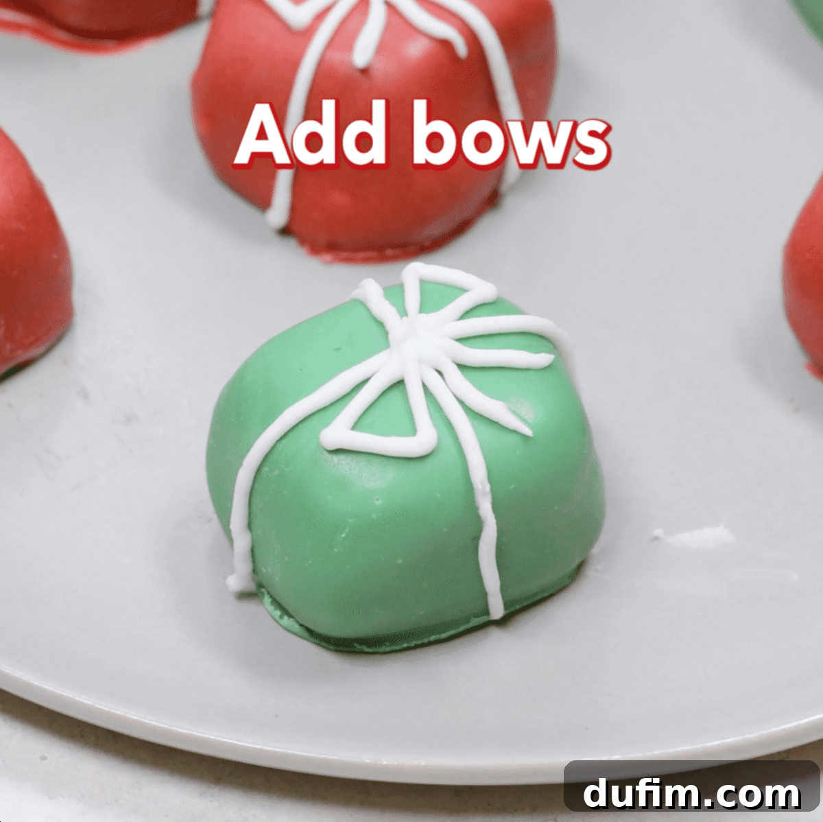 Close-up of a white bow being piped onto a red Christmas present Oreo ball, showcasing the intricate decorating process.