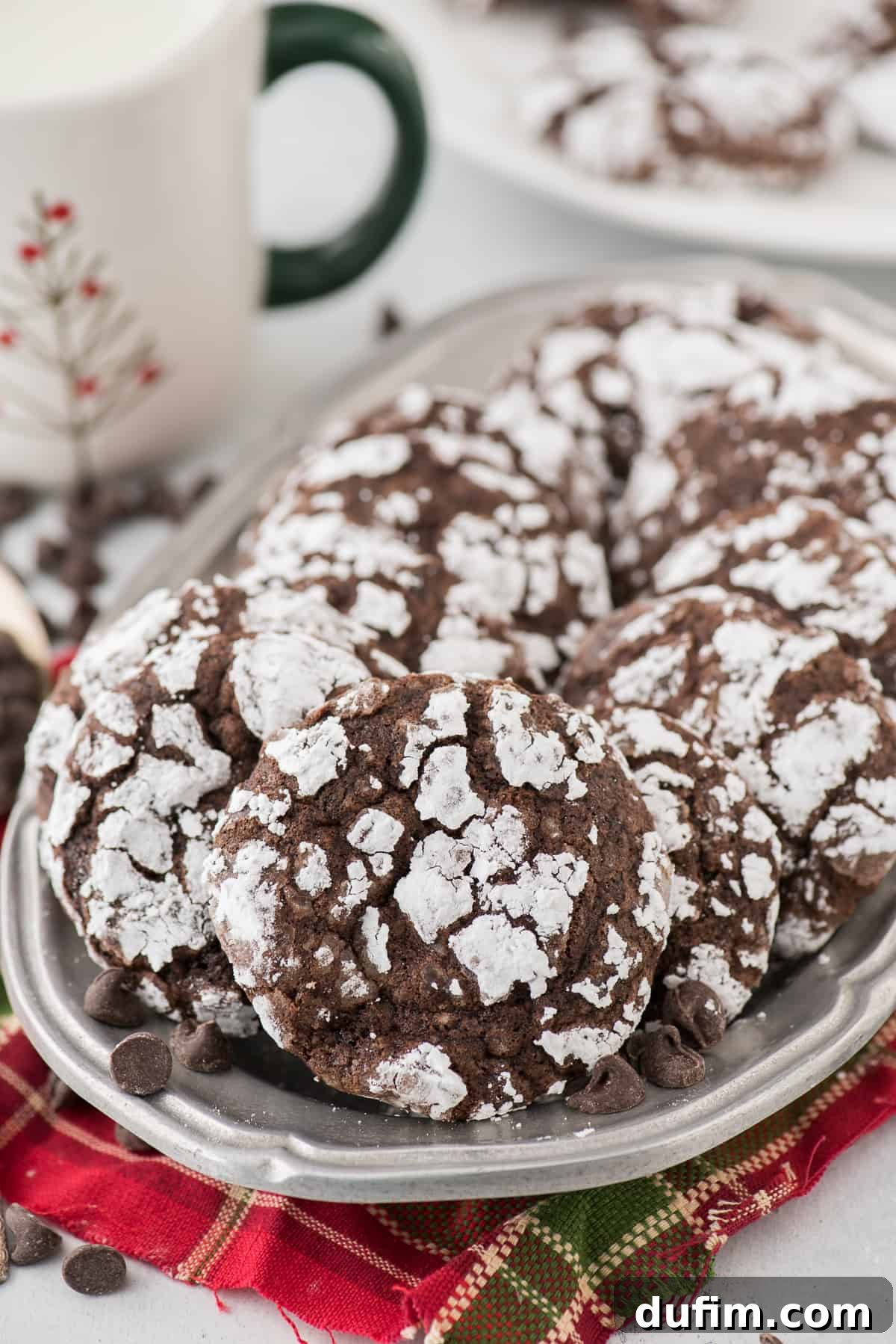 Fudgy Crinkle Delights 2 Fudgy chocolate crinkle cookies generously rolled in powdered sugar, beautifully arranged on a rustic metal tray with a festive red towel peeking out from underneath.