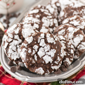 A silver tray filled with freshly baked chocolate crinkle cookies, heavily coated in powdered sugar, resting on a festive red and green cloth.