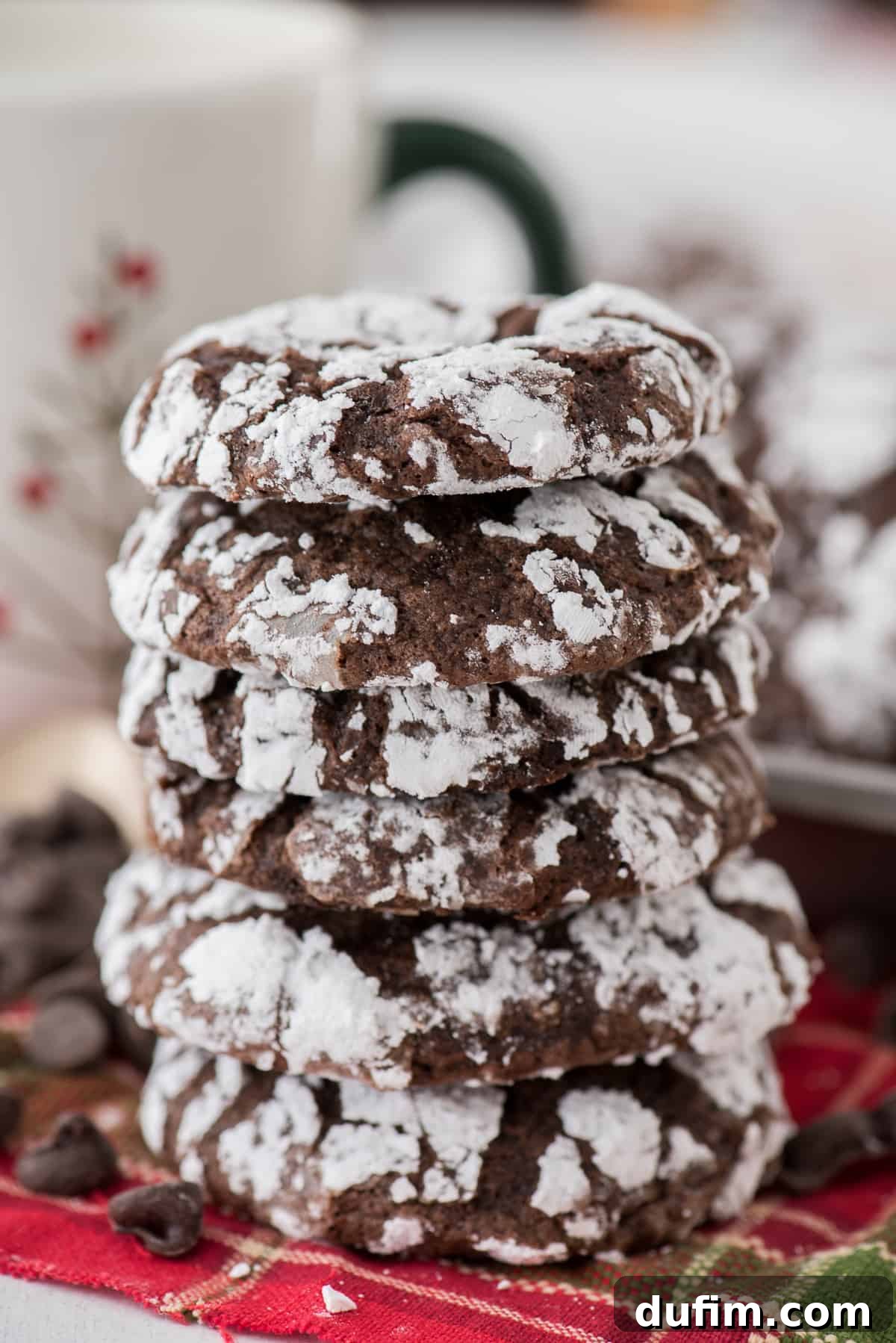 Fudgy Crinkle Delights 3 Stack of freshly baked chocolate crinkle cookies, coated in powdered sugar, resting on a vibrant red towel, showcasing their perfect texture and festive appeal.