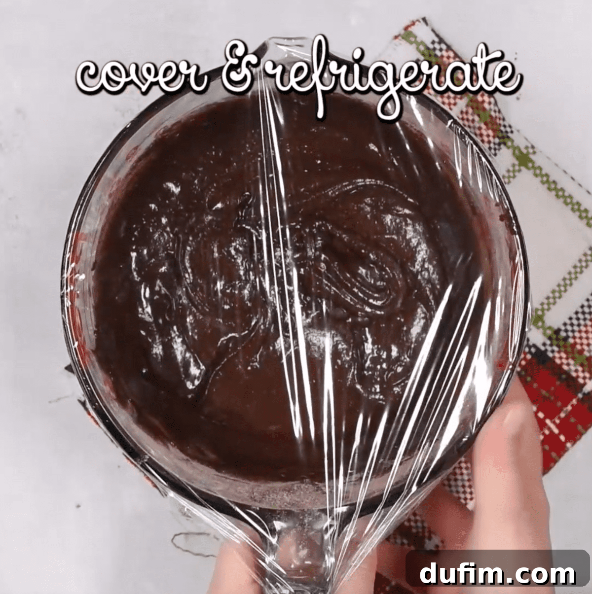 Fudgy Crinkle Delights 7 A bowl of chocolate cookie dough covered tightly with plastic wrap, being prepared for refrigeration.
