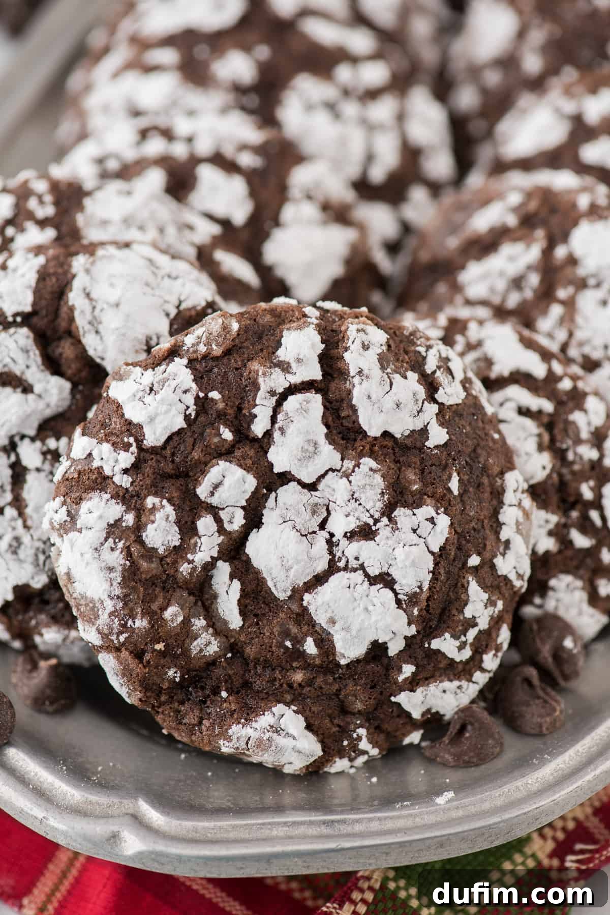 Fudgy Crinkle Delights 8 Freshly baked chocolate crinkle cookies, perfectly cracked and coated in powdered sugar, cooling on a metal baking tray with a red towel draped nearby.