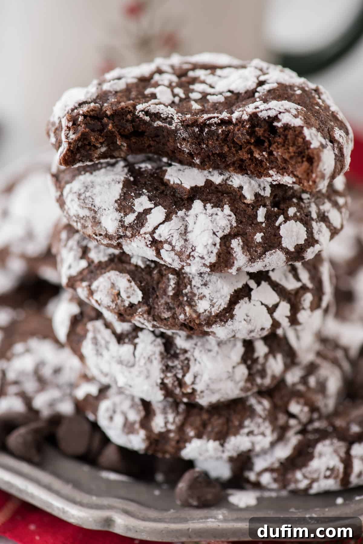 Fudgy Crinkle Delights 9 A stack of delicious chocolate crinkle cookies, each covered in powdered sugar, artfully arranged on a sleek metal plate.