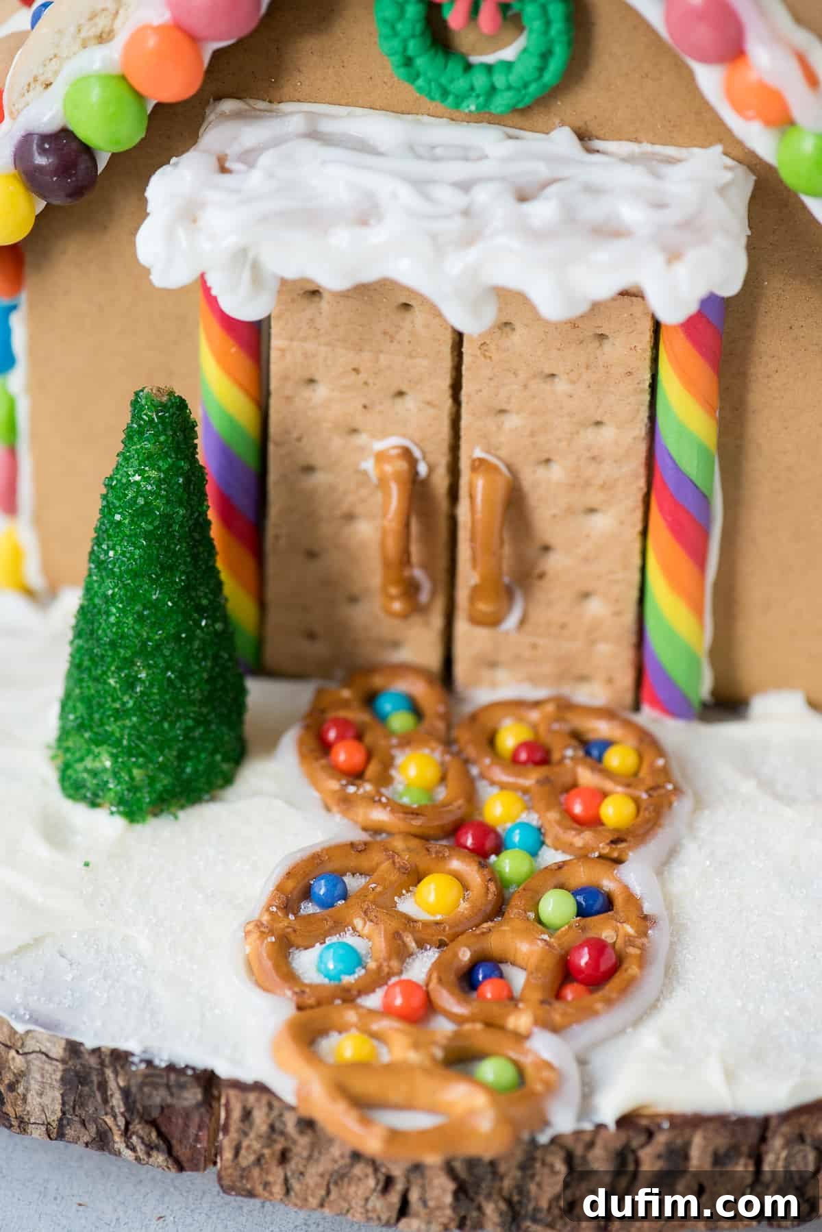 Hands carefully placing colorful candies on a gingerbread house roof, showcasing the creative process.